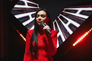 Kırmızı elbiseli genç bir kadın sahnede gösteri yapıyor. Bir müzik konseri sırasında elinde mikrofon tutan şarkıcı.