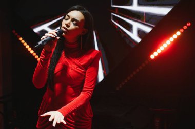 Sahnede kırmızı ışıklar altında duygusal ve tutkulu bir ses performansı sergileyen bir kadın şarkıcı.