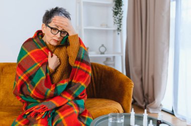 Yetişkin bir kadın evde dinlenirken sıcak bir battaniyeye sarılmış baş ağrısı ve ateşle kendini iyi hissetmiyor.