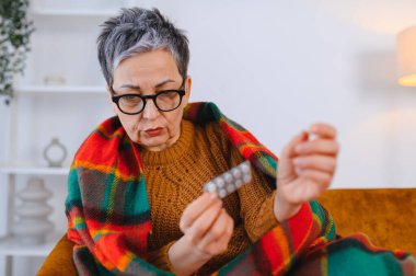 Yaşlı kadın kendini iyi hissetmiyor. Soğuk algınlığı veya grip için bir paket hap tutuyor.