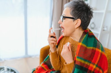 Kadın kendini iyi hissetmiyor, nezle ya da grip. Evde dinlenirken boğaz spreyi kullanıyor.