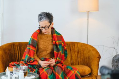 Yaşlı kadın hastalıktan muzdarip, sıcak bir battaniyenin altında kendini hasta hissediyor, grip ve baş ağrısı belirtileri gösteriyor.