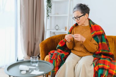 Yaşlı kadın kendini iyi hissetmiyor. Elinde baş ağrısı veya migren için ilaç dolu bir paket var.