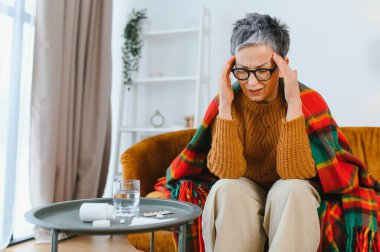 Baş ağrısı ya da migrenden muzdarip yaşlı bir kadın kendini iyi hissetmiyor ve su ve ilaçla rahatlamak istiyor.