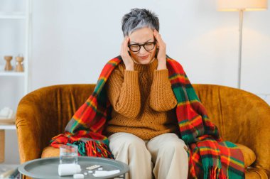 Şiddetli migrenden muzdarip, başı ağrıyan yaşlı bir kadın. İlaçlar ve su kullanıma hazır bir masada oturur.