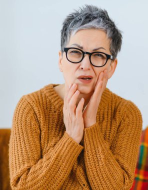 Şiddetli diş ağrısı çeken, yüzünü buruşturan ve yanağını tutarak rahatsızlığını dile getiren ve oral sağlık yardımına ihtiyaç duyan bir kadın.