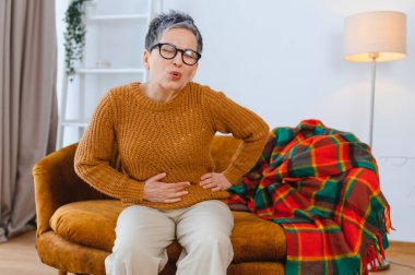 Şiddetli karın ağrısı çeken yaşlı bir kadın, karnını tutuyor, rahatsızlık ve ıstırap gösteriyor.