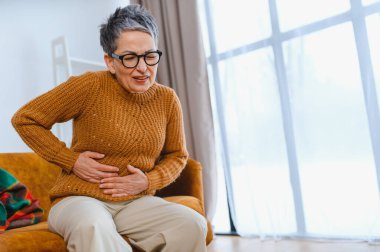 Yaşlı kadın evde otururken mide ağrısı, hazımsızlık ve kramplar çekiyor. Rahatlamaya ihtiyacı var.