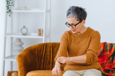 Yaşlı kadın cilt alerjisi, kaşıntı ve tahriş, evde otururken kolunu kaşıyor.
