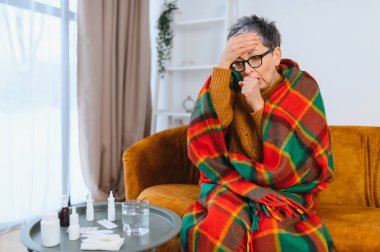 Sıcak bir battaniyenin altında yatarken ateşi, öksürüğü ve baş ağrısı olan son sınıf öğrencisi bir kadın. İlaçlar masada.