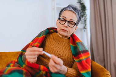 Yaşlı kadın soğuk algınlığı, grip ya da mevsimsel hastalıktan muzdarip. Vücut ısısını kontrol ediyor, evde kendini kötü hissediyor.