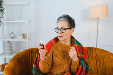 Soğuk algınlığı için boğaz spreyi kullanan ya da sıcak bir battaniyeye sarılı grip belirtileri gösteren bir kadın kendini kötü hissediyor.