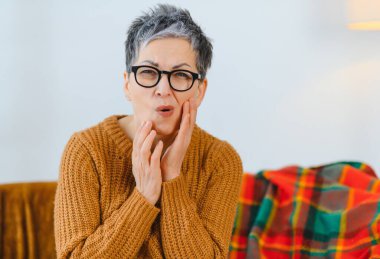 Diş ağrısından muzdarip yaşlı bir kadın, iki eliyle yanağını tutuyor, acil ağız bakımına ihtiyacı var.