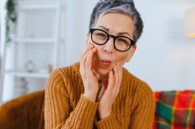 Diş ağrısı çeken yaşlı bir kadın, şişmiş yanağını tutuyor. Rahatsızlık ve oral sağlık sorunları