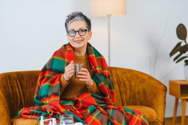 Son sınıf öğrencisi, sıcak bir battaniyeye sarılı olarak kanepede dinleniyor, sıcak çay içerken evde grip oluyor.