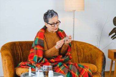 Yaşlı kadın sıcak bir battaniyeye sarılmış elinde bir paket hapla, soğuk algınlığıyla kendini hasta hissediyordu.