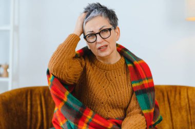 Yaşlı kadın kendini kötü hissediyor, battaniyeye sarılmış, kanepede baş ağrısı çekiyor. Stres ve hastalık kavramı