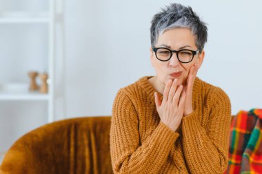 Diş ağrısından muzdarip son sınıf öğrencisi. Kapalı alanda yüzünü buruşturan bir ifadeyle yanağını tutuyor. Oral sağlık rahatsızlığı kavramı