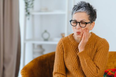 Şiddetli diş ağrısından suratını buruşturan, yanağına dokunan, ağız sağlığına ve rahatsızlıktan korunmaya ihtiyacı olan olgun bir kadın.
