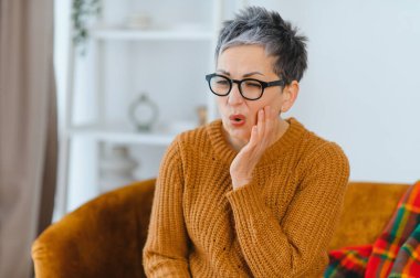 Evde koltukta oturan olgun bir kadın çene ağrısı, acil diş ağrısı ve yardıma ihtiyacı olan diş ağrısı çekiyor.