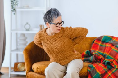 Olgun bir kadın evinde rahatsızlık hissediyor ve beline dokunuyor. Bu da kronik ağrı ya da sağlık sorunlarına işaret ediyor.
