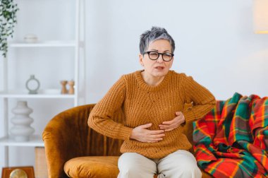 Evdeki kanepede otururken göğüs ağrısı çeken son sınıf öğrencisi bir kadın, acil bir sağlık durumu olduğunu gösteriyor.