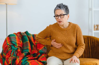 Şiddetli göğüs ağrısı çeken yaşlı bir kadın, yan tarafını rahatsızlık içinde tutuyor. Tıbbi yardım gerektiren bir sağlık sorunu.