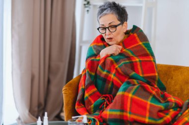 Yaşlı kadın grip ya da soğuk algınlığı semptomları yüzünden kendini iyi hissetmiyor. Sıcak bir battaniyeye sarılıp iyileşmek için evde kalıyor.