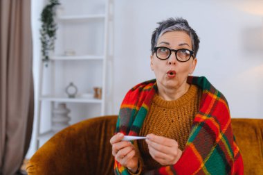 Soğuk algınlığı ya da grip belirtileri gösteren bir kadın. Vücut ısısını dijital termometreyle ölçüyor.