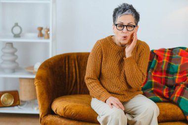 Olgun bir kadın yoğun diş ağrısı çekiyor, yüzünü buruşturuyor ve evde yanağını tutuyor. Ağız sağlığı sorunları var