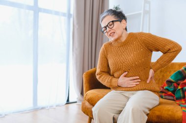 Evde bir kanepede otururken karın ağrısı ve krampları olan yaşlı bir kadın kendini hasta hissediyor.