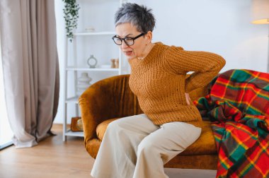 Yaşlı kadın oturma odasındaki kanepede otururken belinde rahatsızlık ve ağrı hissediyor.
