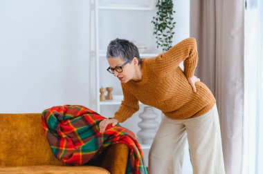 Olgun bir kadın evdeki bel bölgesinde şiddetli bir rahatsızlık yaşıyor, kronik sırt ağrısı ve sağlık sorunlarıyla boğuşuyor.