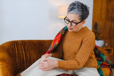 Kanepede oturan yaşlı bir kadın diz eklem ağrısı, eklem iltihabı ve bacağındaki rahatsızlıktan muzdarip.