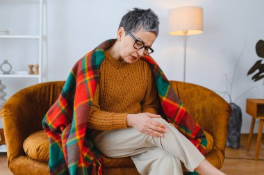 Evde otururken kronik diz ağrısı çeken yaşlı bir kadın, eklem rahatsızlığı için rahatlamaya ihtiyacı var.