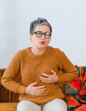 Rahatsızlık hisseden ve göğsünü ve karnını tutan bir kadın. Sağlık sorunu ya da kalp ağrısına işaret ediyor.