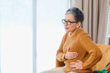 Ağır göğüs ağrısı çeken yaşlı bir kadın. Göğsünü evde tutuyor. Sağlık sorunları, kalp krizi belirtileri