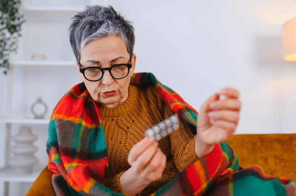 Yaşlı kadın kendini iyi hissetmiyor. Soğuk algınlığı veya grip için bir paket hap tutuyor.