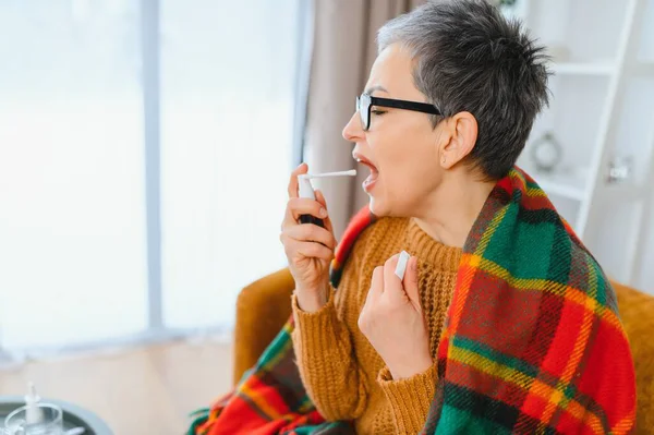 Kadın kendini iyi hissetmiyor, nezle ya da grip. Evde dinlenirken boğaz spreyi kullanıyor.