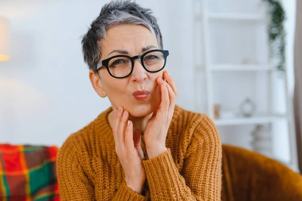 Şiddetli diş ağrısı çeken, yüzünü buruşturan ve yanaklarını tutan bir kadın oral rahatsızlığı ya da diş problemini işaret ediyor.