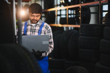 Genç Hintli tamirci bir lastik tamirhanesinde ya da depoda dizüstü bilgisayardan siparişleri kontrol edip işine odaklanıyor.