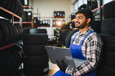 Tulumlu sakallı tamirci stokları kontrol etmek ve otomotiv ve onarım için envanteri yönetmek için bir lastik dükkanında dizüstü bilgisayar kullanıyor.