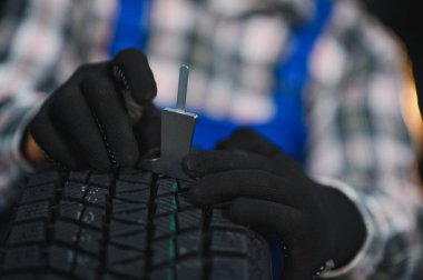 Siyah eldivenli bir adam araba tamirhanesinde araç güvenliğini ve bakımını sağlamak için lastik izlerini derinlik göstergesiyle kontrol ediyor.