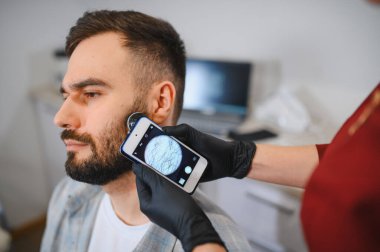 Trikoloğum, bir klinikte saç kaybını ve deri durumunu teşhis etmek için trikop ile hastanın kafa derisini ve saçını inceliyor.