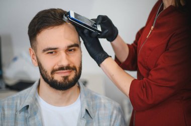 Trikoskopi sırasında gülümseyen erkek hasta, bir uzmanla kafa sağlığı ve saç kaybı endişelerini değerlendiriyor.