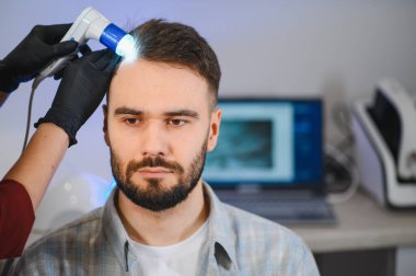 Erkek hasta, saç dökülmesi ve diğer dermatolojik durumları teşhis etmek için kafa derisini trikobik bir muayeneden geçiriyor.