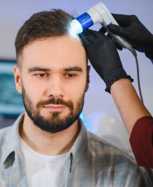 Trikoloğum bir adamın kafa derisini modern bir trikop ile inceliyor, saç kaybını teşhis ediyor ve özel bir sağlık hizmeti sağlıyor.