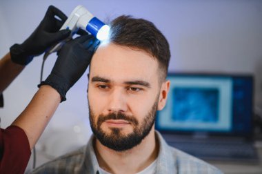 Dermatolog saç sağlığı, saç dökülmesi ve saç büyümesi için trikop kullanarak erkek hastanın kafa derisini inceliyor.