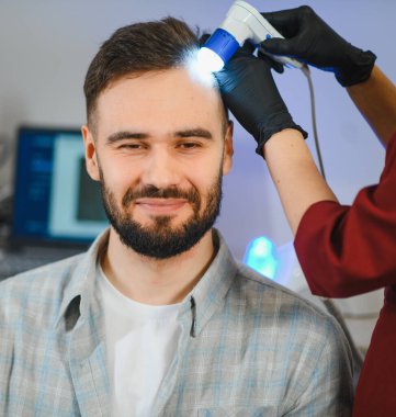 Trikoskopi sırasında gülümseyen bir adam, sağlık ve saç kaybını profesyonel bir doktorla değerlendiriyor.