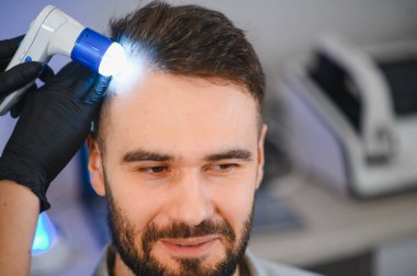 Trikoloğun kafa derisi ve saç foliküllerinin analizini alan adam saç kaybını ve olası tedavileri kontrol ediyor.